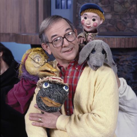 Ernie Coombs in a yellow sweater surrounded by puppets.