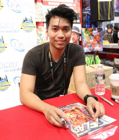 Francis Manapul in a t-shirt sitting at a table with a comic in front of him.