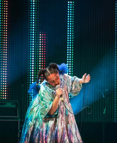 Lido Pimienta in colourful costume performing onstage.