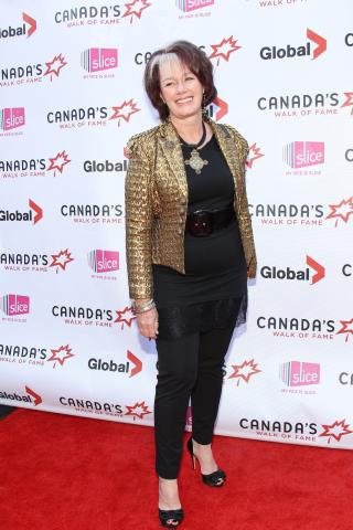A woman in a gold jacket over a black outfit poses on the red carpet.