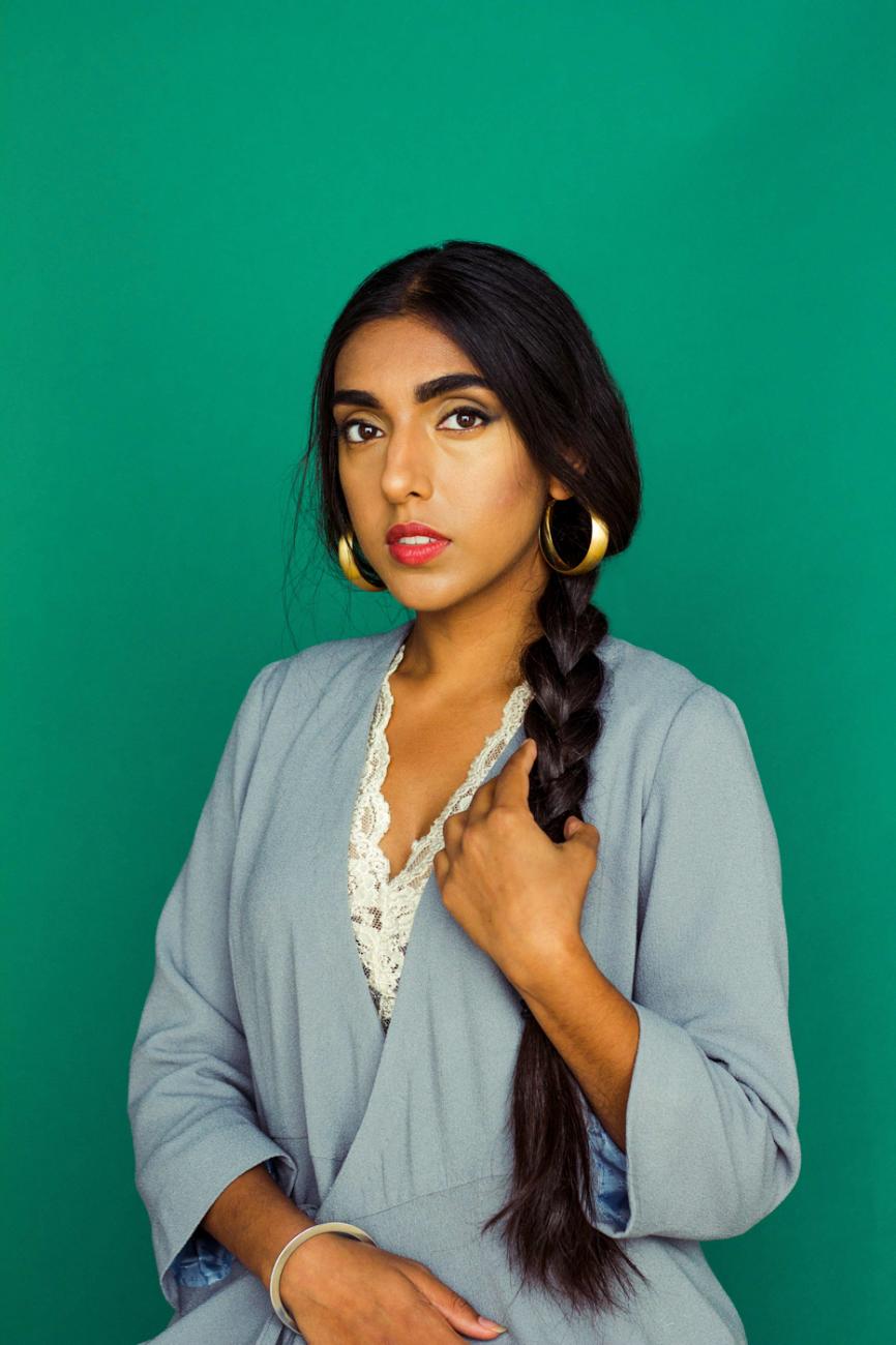 Portrait photo of Rupi Kaur dressed in pale blue with a long braid and a green background.