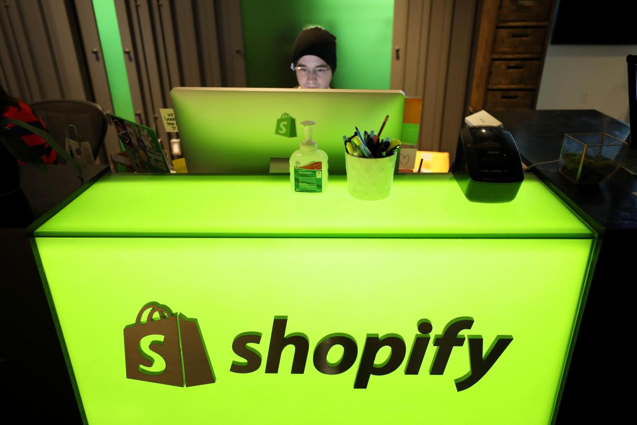 Man looking at a screen behind a green backlit desk with the Shopify logo.