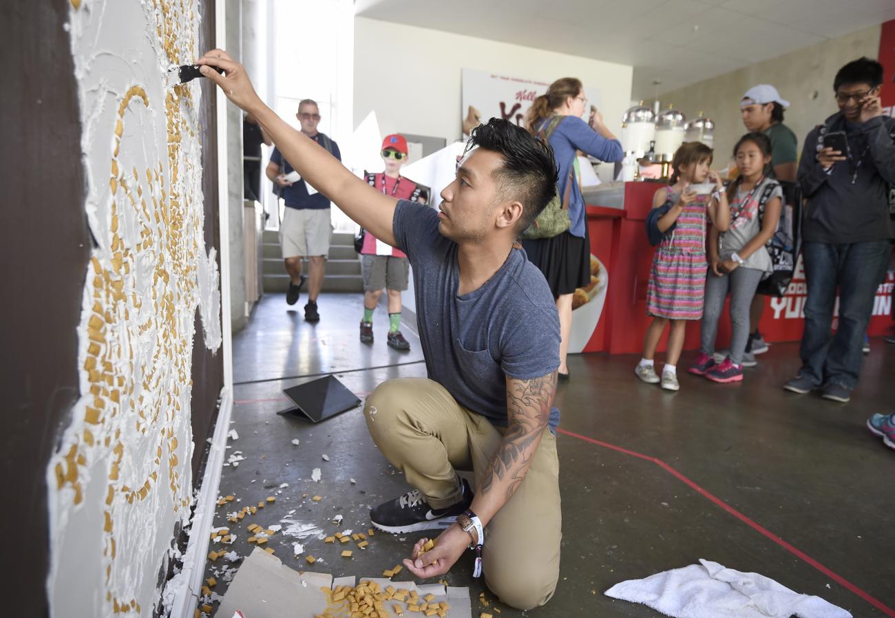 Francis Manapul kneeling and adding cereal to a piece of wall art.