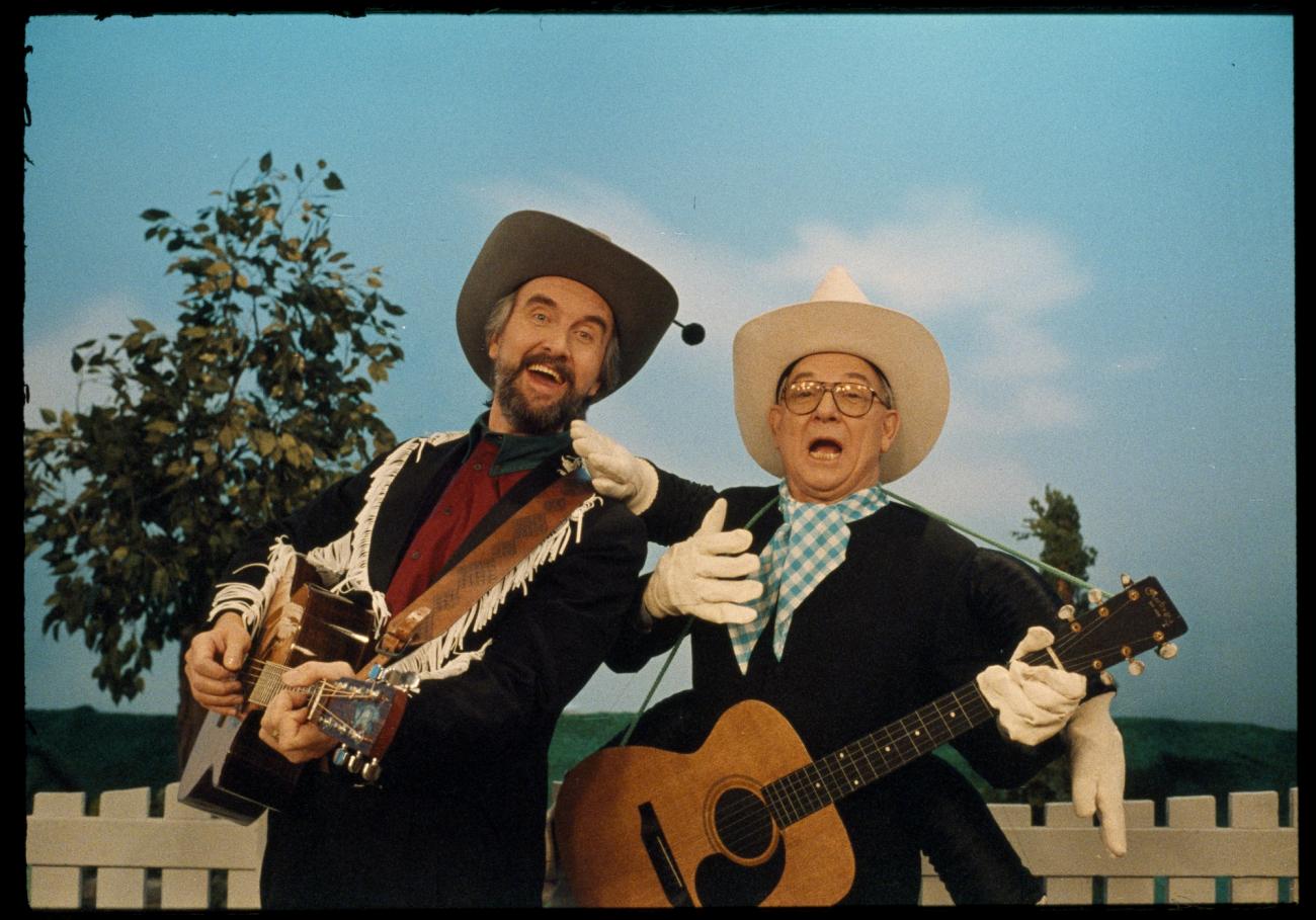 Ernie Coombs and another man with guitars, both wearing Stetsons and dressed in a Western style.
