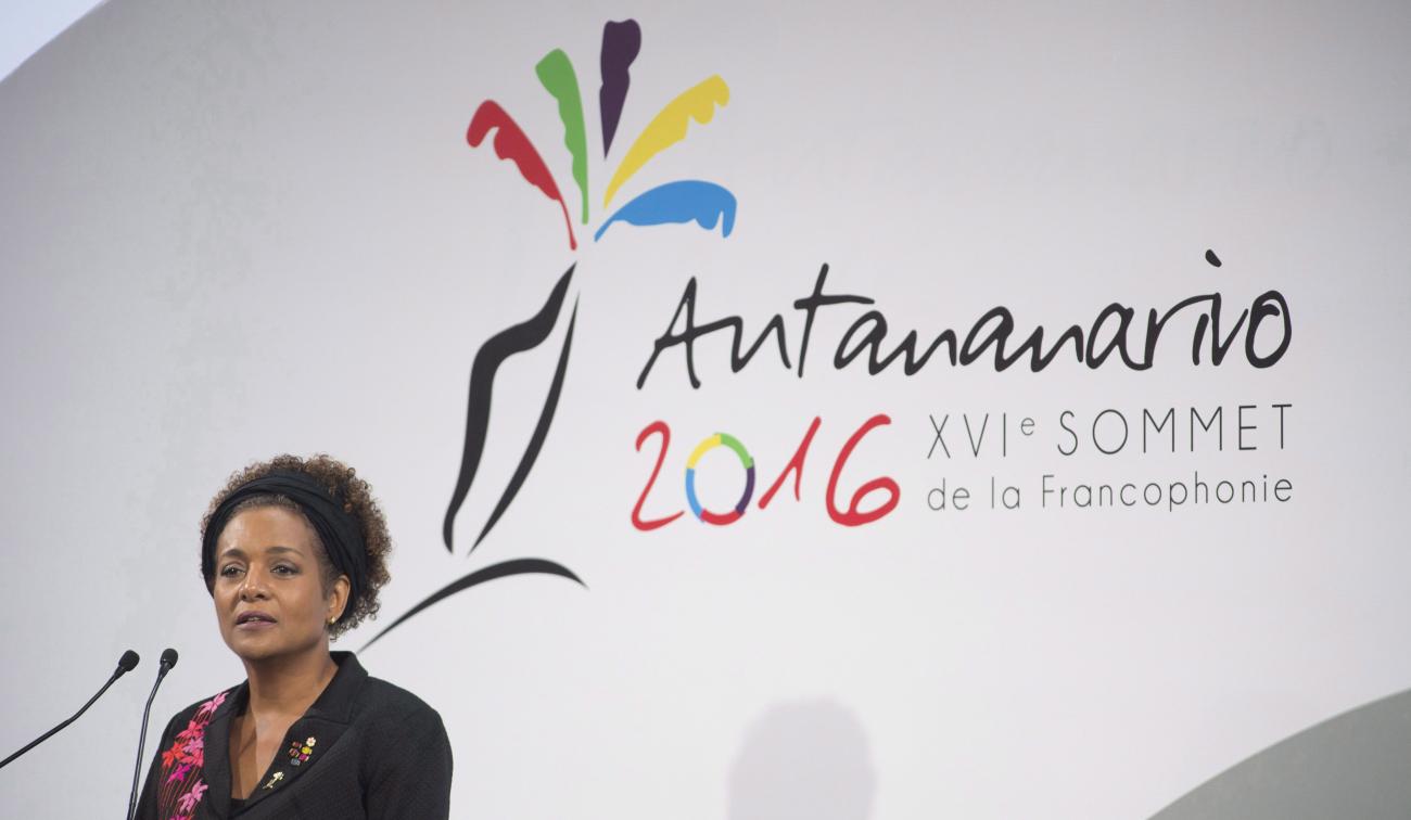 Michaëlle Jean on stage at a microphone with a conference banner behind.