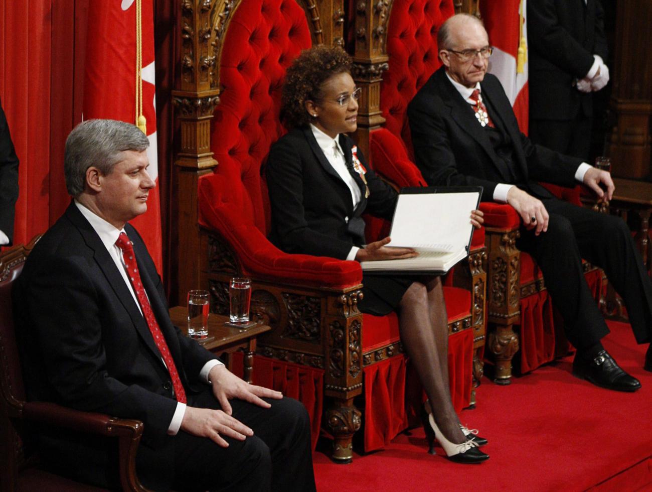 Michaëlle Jean sitting on a red throne between two men, one on a red throne, the other on a chair.
