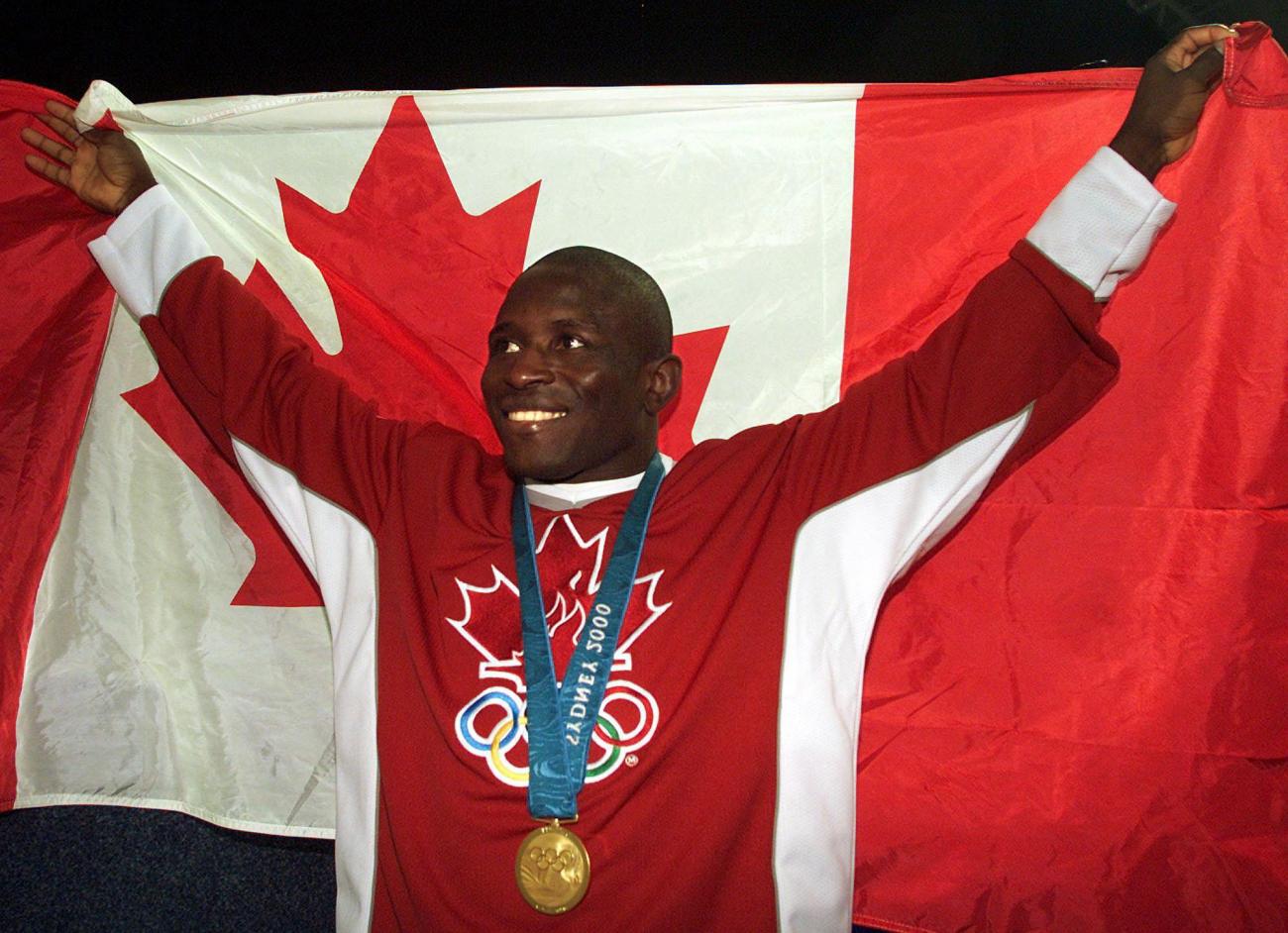 Daniel Igali dressed in red wearing a medal holding a Canadian flag behind him.
