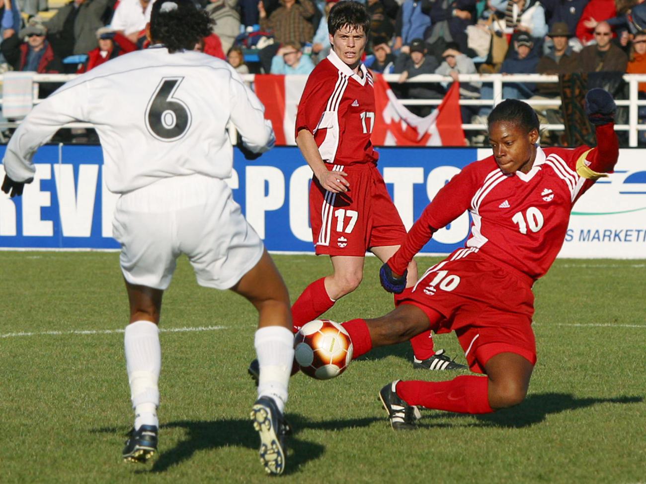 Charmaine Hooper in red on soccer field with two other players, one in red, the other in white.