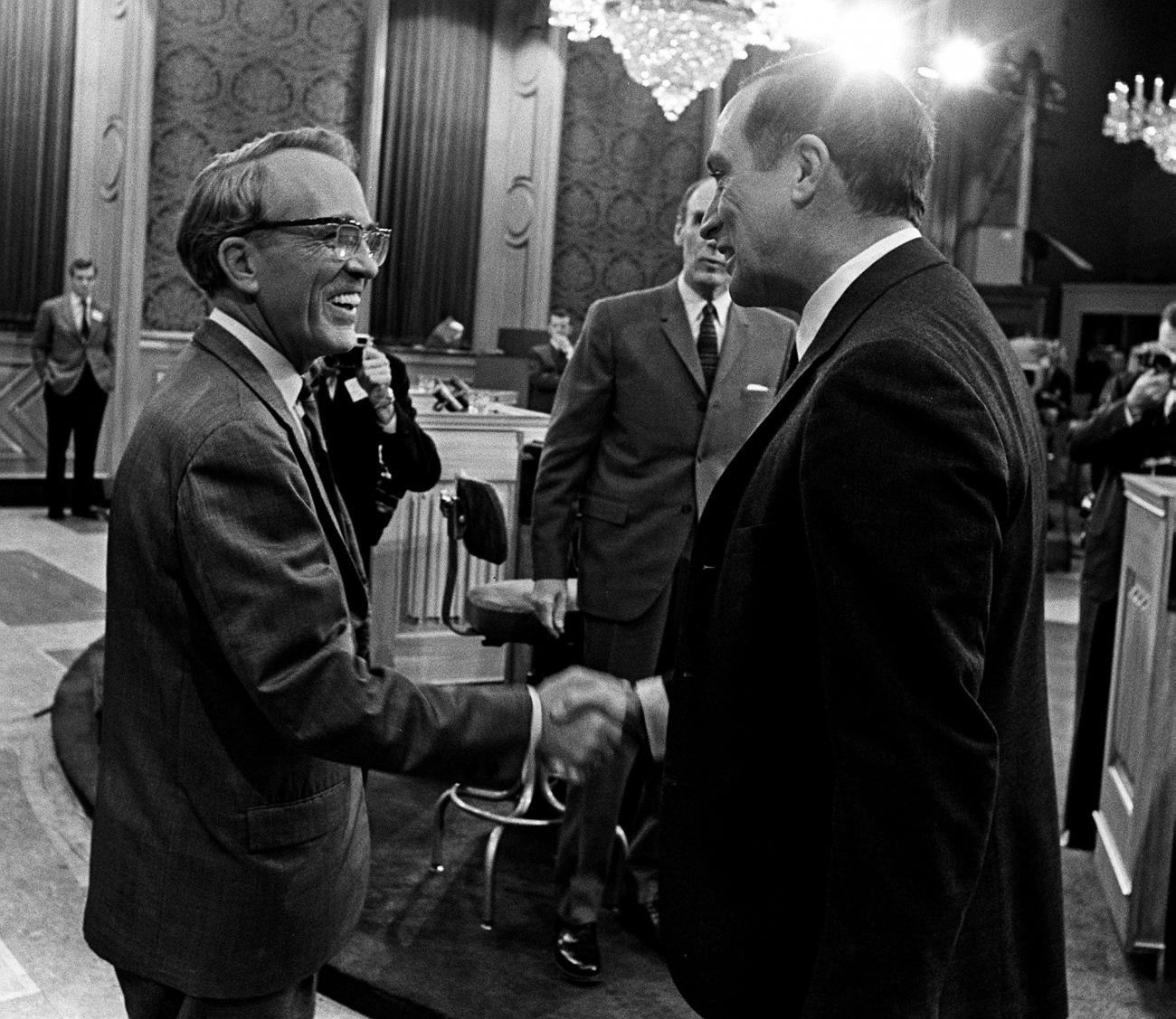 Tommy Douglas and a man both wearing suits are shaking hands.