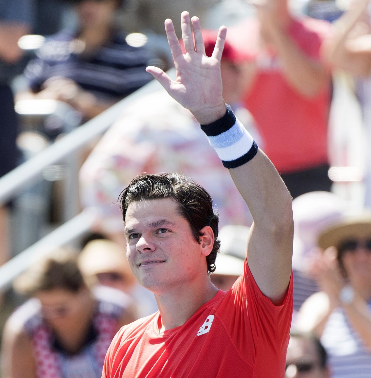 Milos Raonic stand in front of a crowd dressed in red and waving his arm.