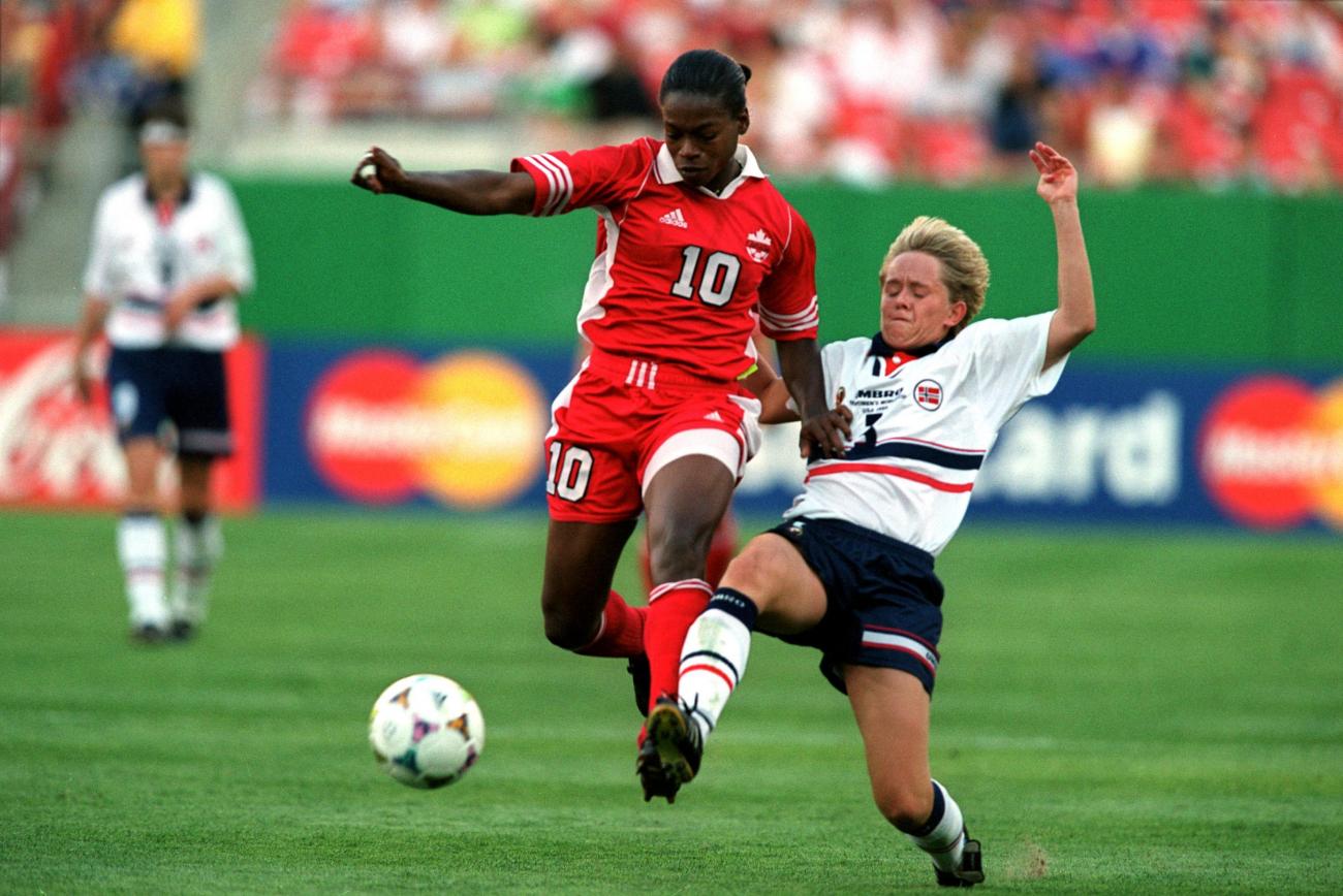 Charmaine Hooper in red and another player in white on soccer pitch going after ball.