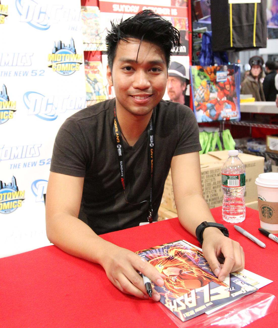 Francis Manapul sat at a desk about to sign a Flash comic.