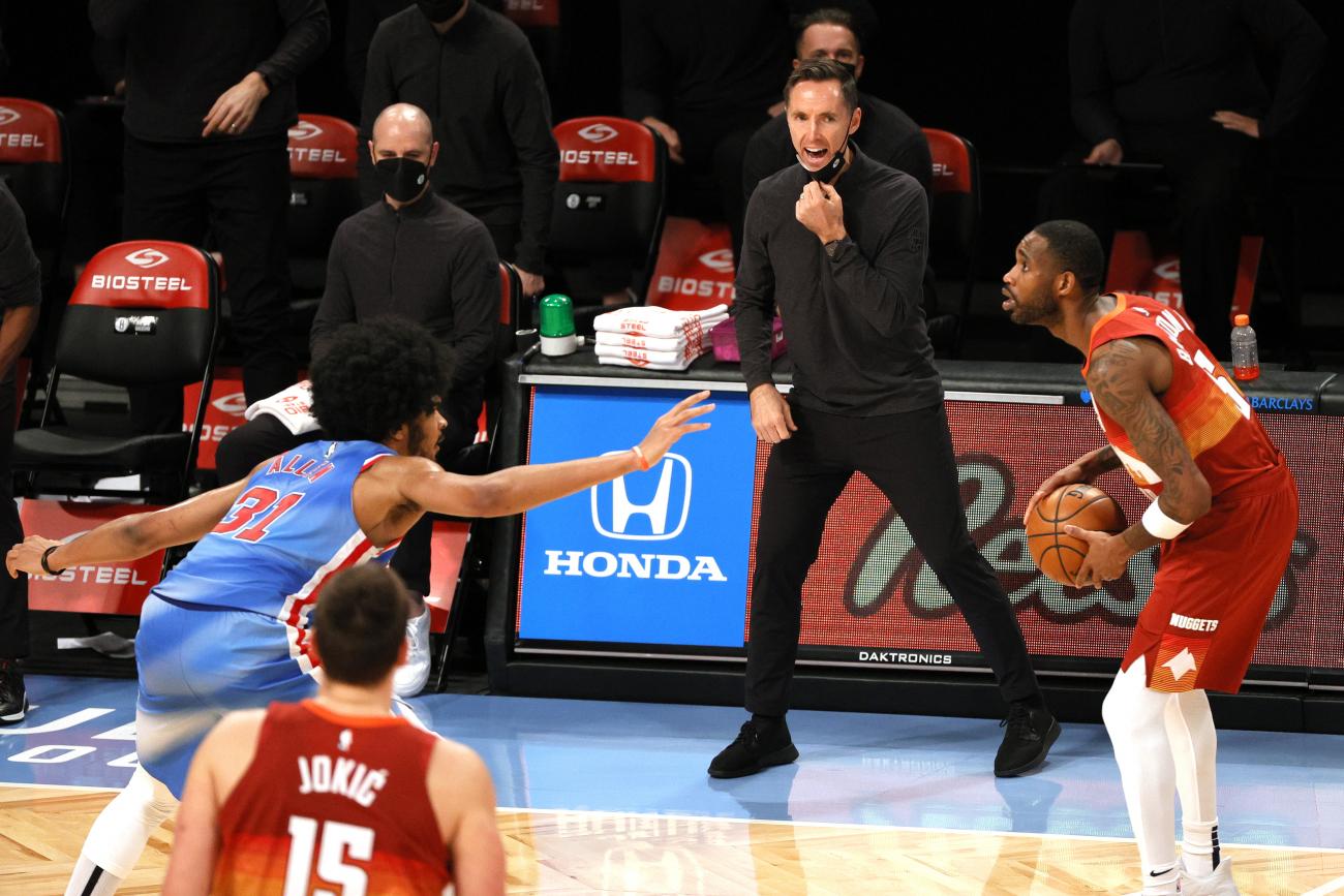 Steve Nash in black stands at the side of a basketball court shouting at players.