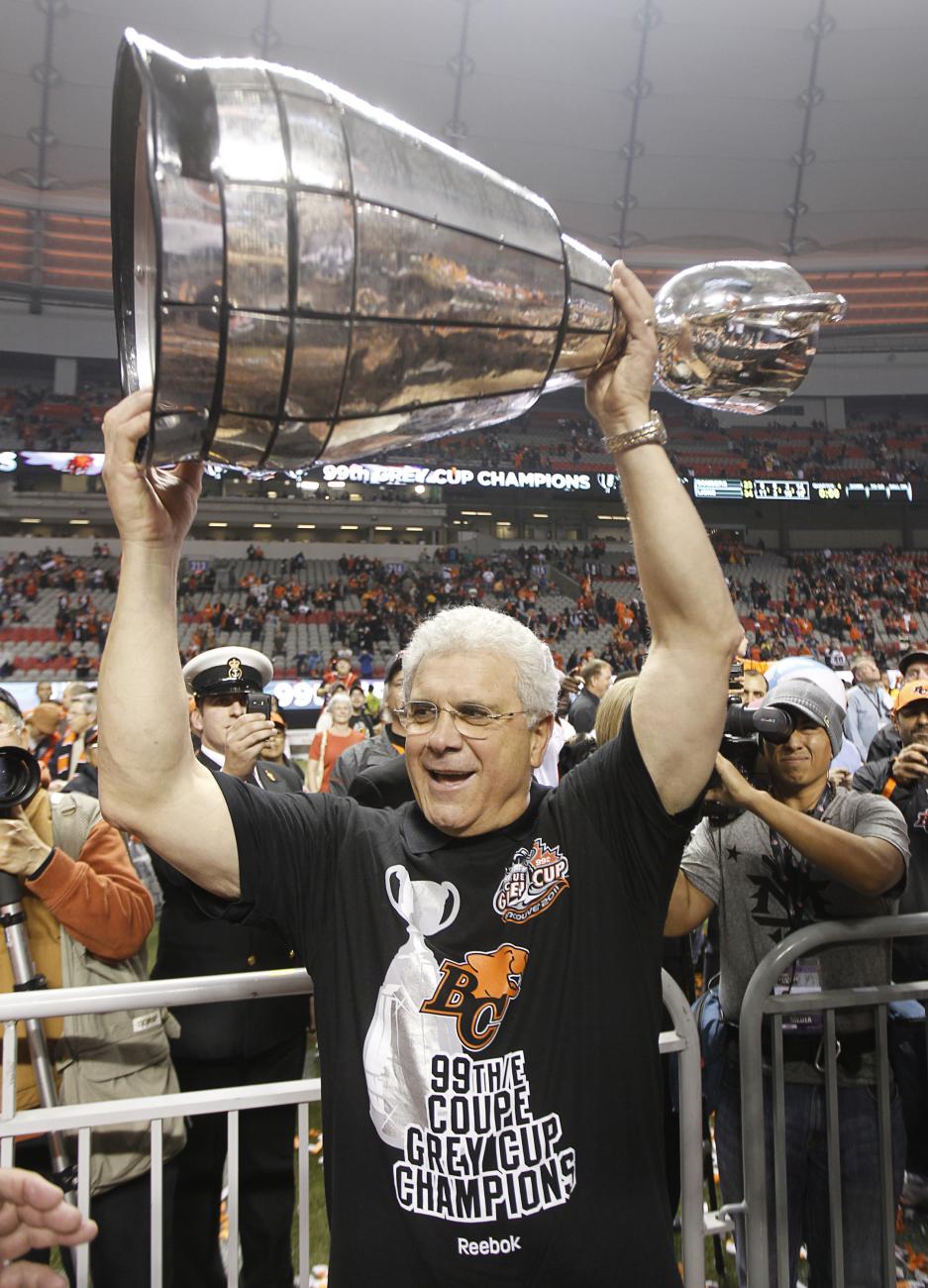 Wally Buono in stadium full of people, holding a large trophy cup above his head.