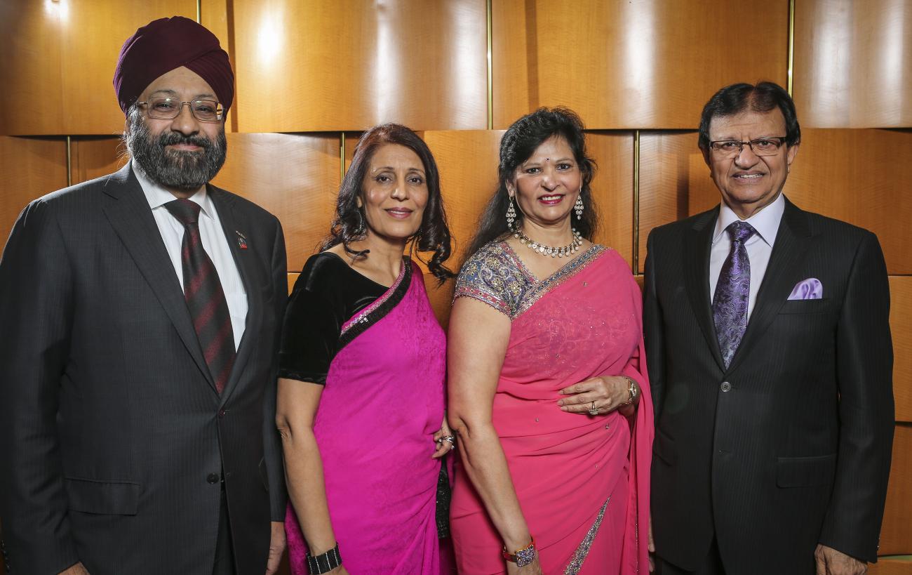 Photo of Steve Gupta in a suit with three people, two women in saris, and a man in a suit wearing a turban.