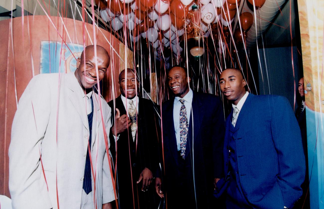 Donovan Bailey and three men stand smiling among ribbons hanging from balloons above them.