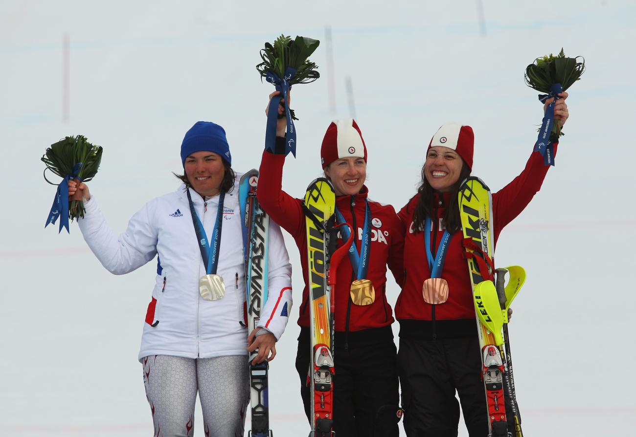 Karolina Wisniewska in red uniform with another woman in red and a woman in white all wearing medals and holding up bouquets.