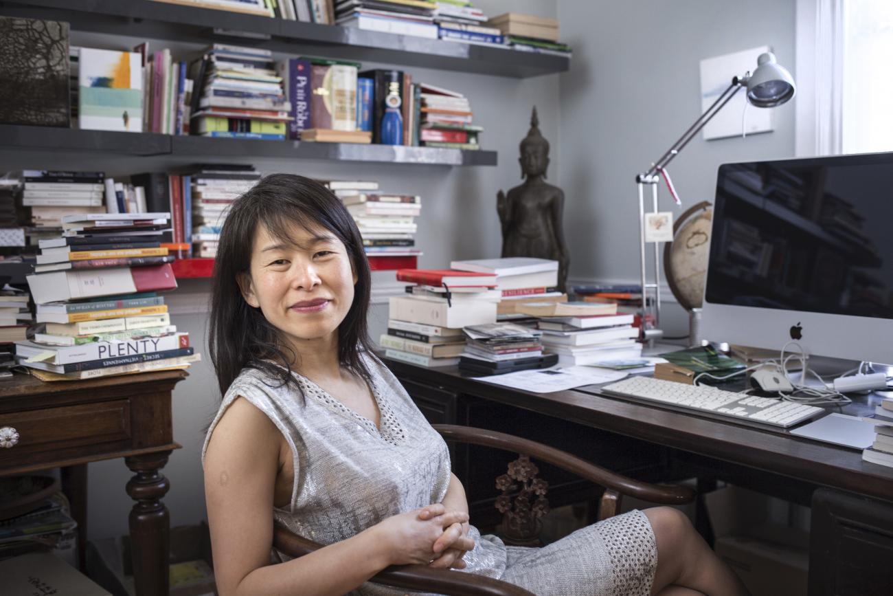 Kim Thúy Ly Thanh sitting at a desk, book shelves behind her.