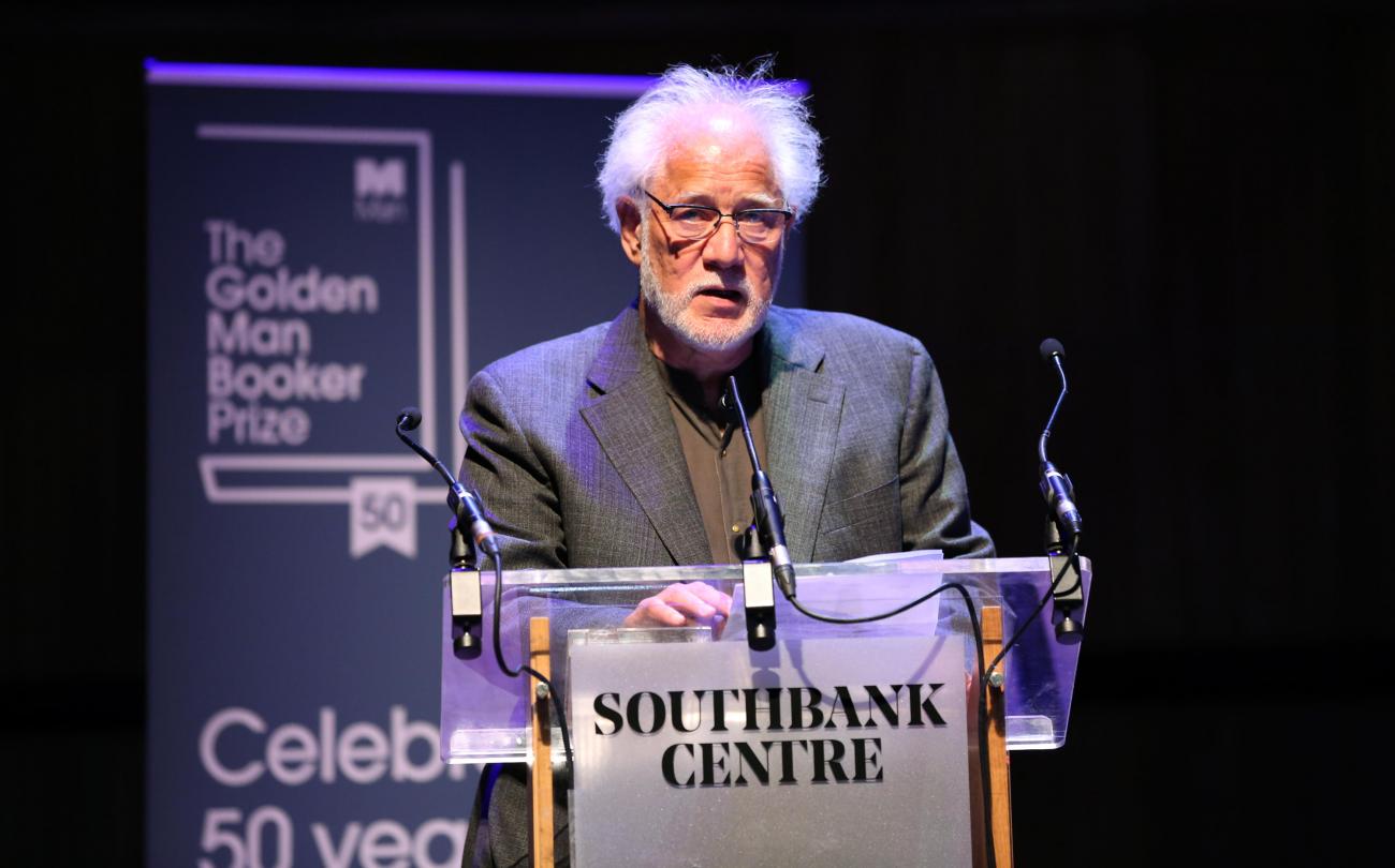 Michael Ondaatje standing at a podium on stage.