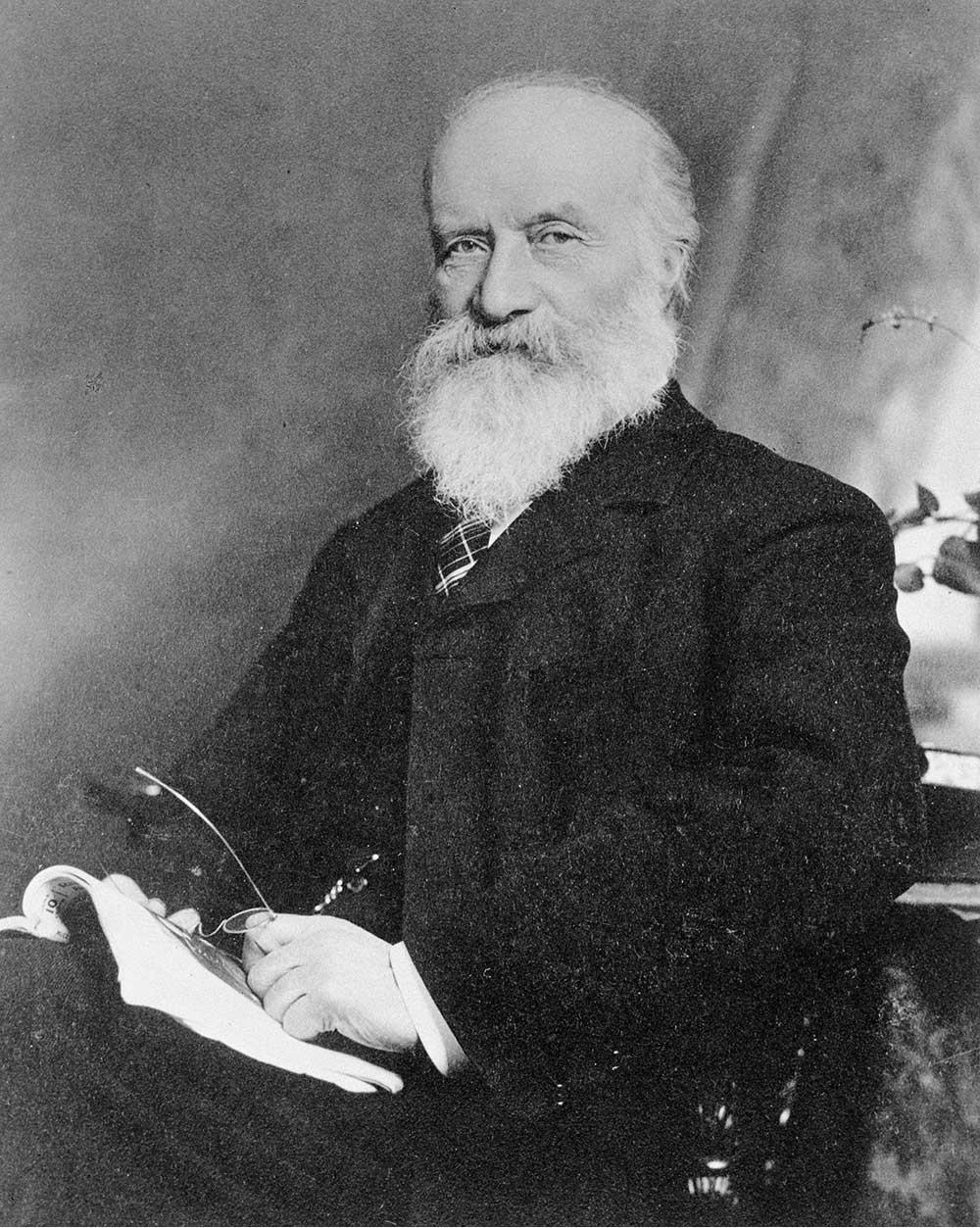 Black and white portrait photo of Sandford Fleming holding his glasses and a book.