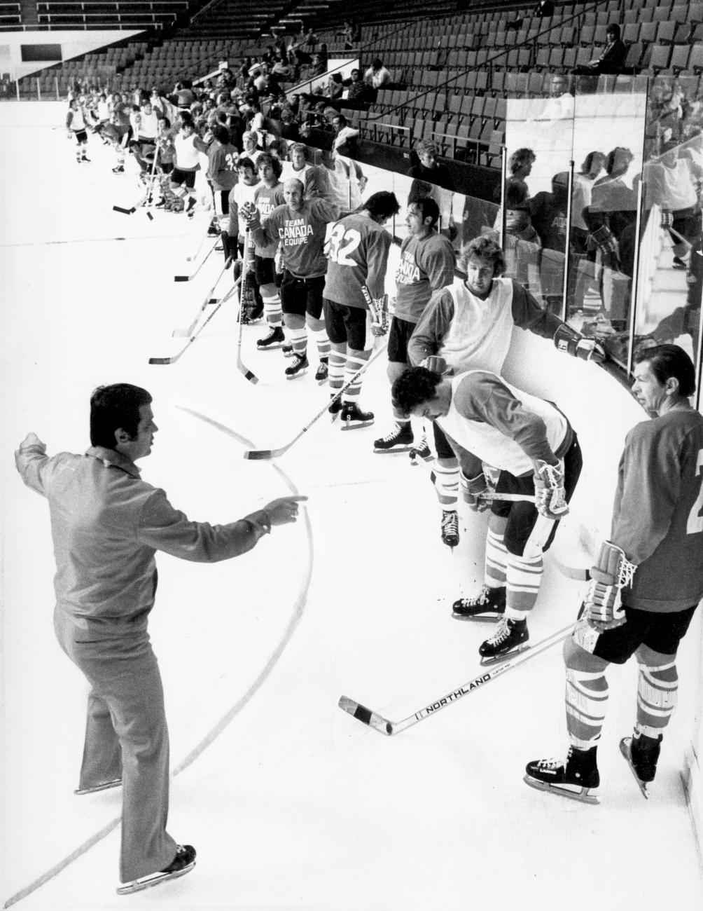 a line of hockey players along the edge of the rink with Stan Mikita talking to the coach in the foreground.