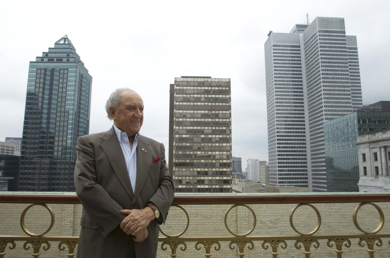 David Azrieli stands in front of three highrise buildings.