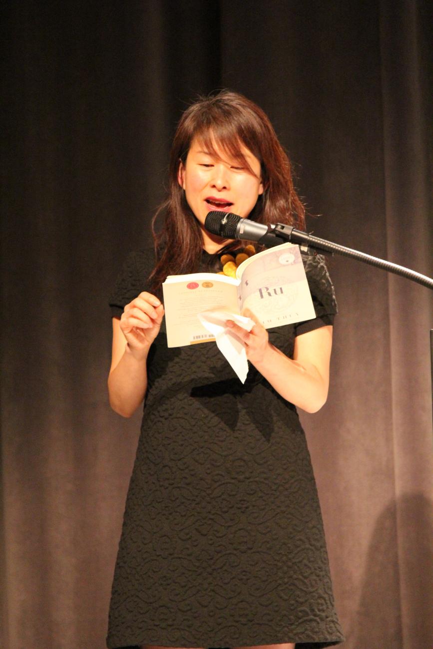 Kim Thuy dressed in black reads from a book on stage.