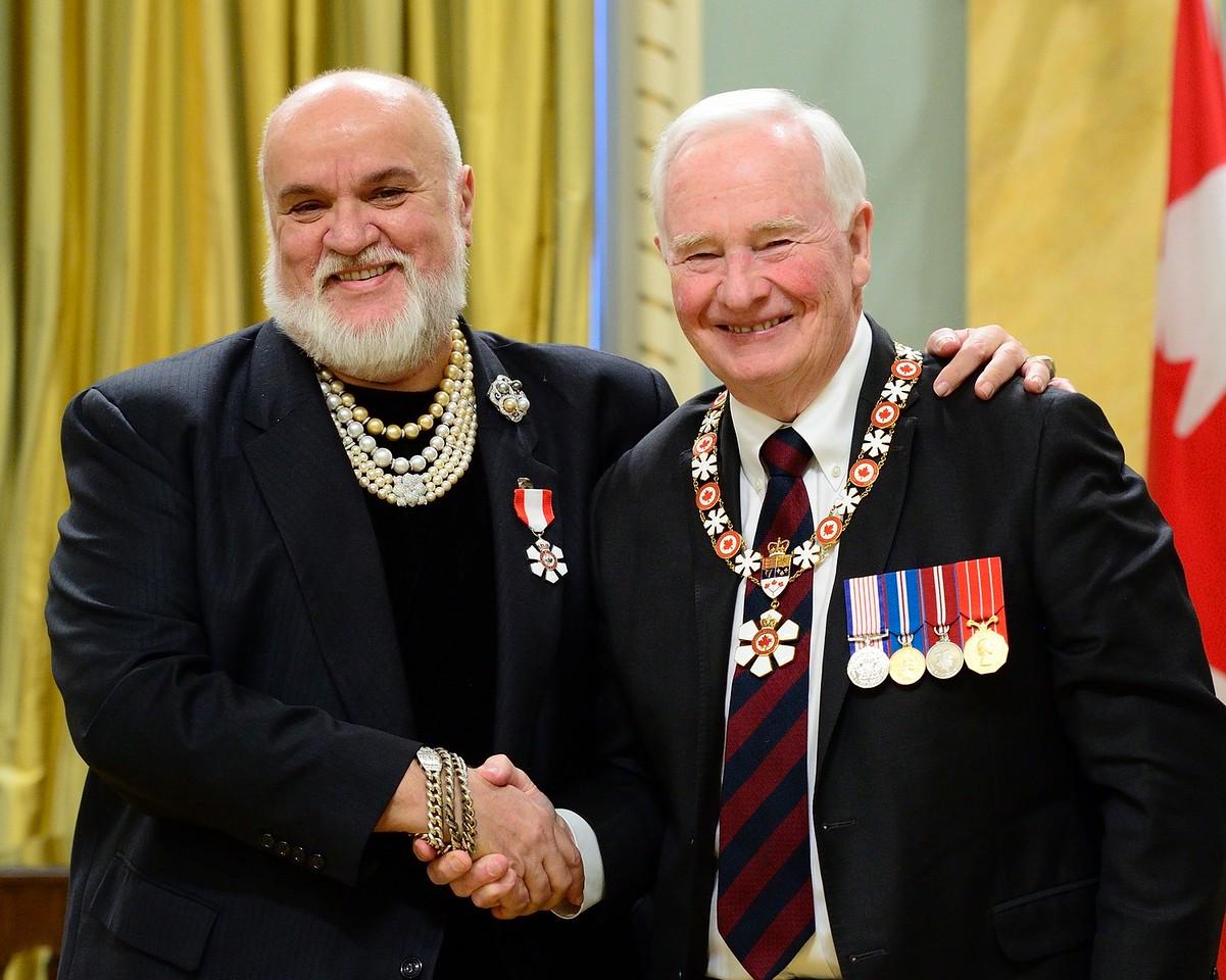 Salah Bachir and Governor General David Johnston shaking hands for a posed photograph wearing medals of honour.