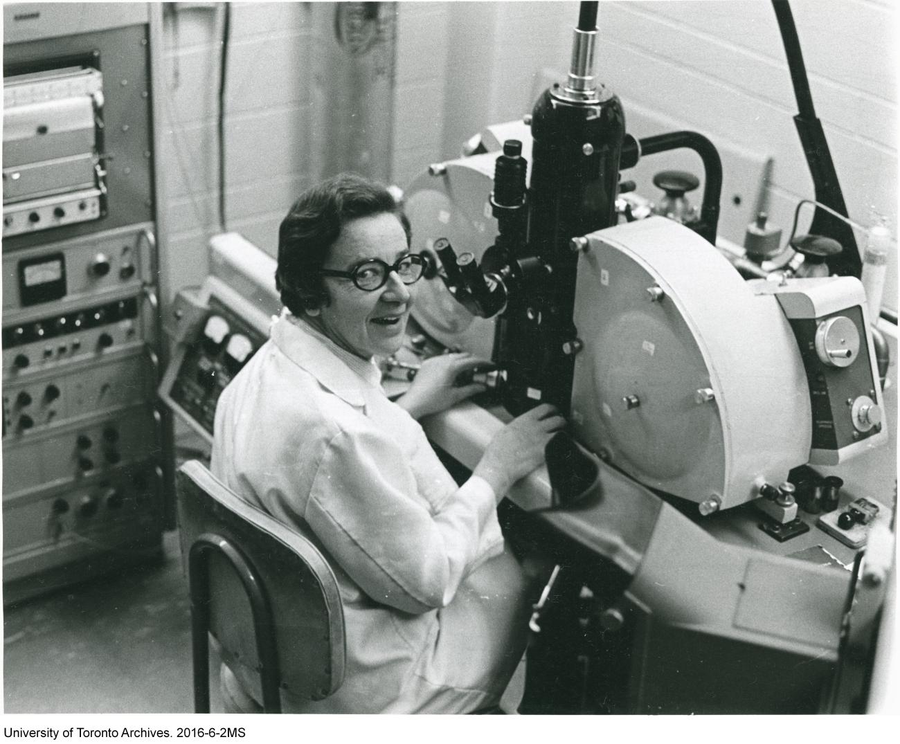 A scientist smiles at the camera from her place in front of a microscope